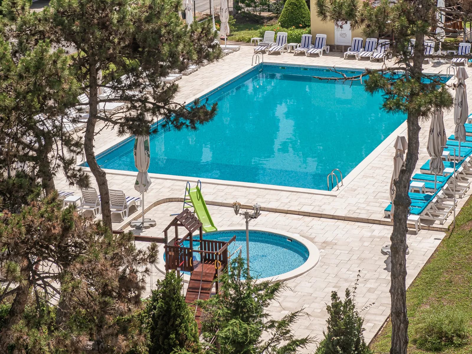 Vedere de la etaj asupra piscinelor, grădinii și locului de joacă ale hotelului